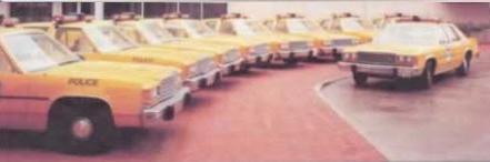 1989 Ford LTD Crown Victoria - A row of yellow police cars, likely 1980s Ford LTD Crown Victoria sedans, parked at an angle with 'POLICE' lettering on the front doors. Th…