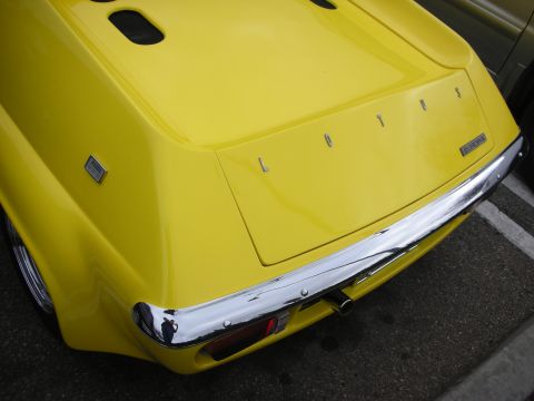1998 Ford Crown Victoria - Close-up of the rear deck and chrome bumper of a yellow Lotus sports car, with spaced-out LOTUS lettering across the tail.