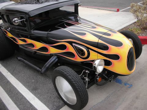 1998 Ford Crown Victoria - Low front three-quarter view of a black hot rod with bold orange flame graphics, a single chrome headlight and an exposed front axle.