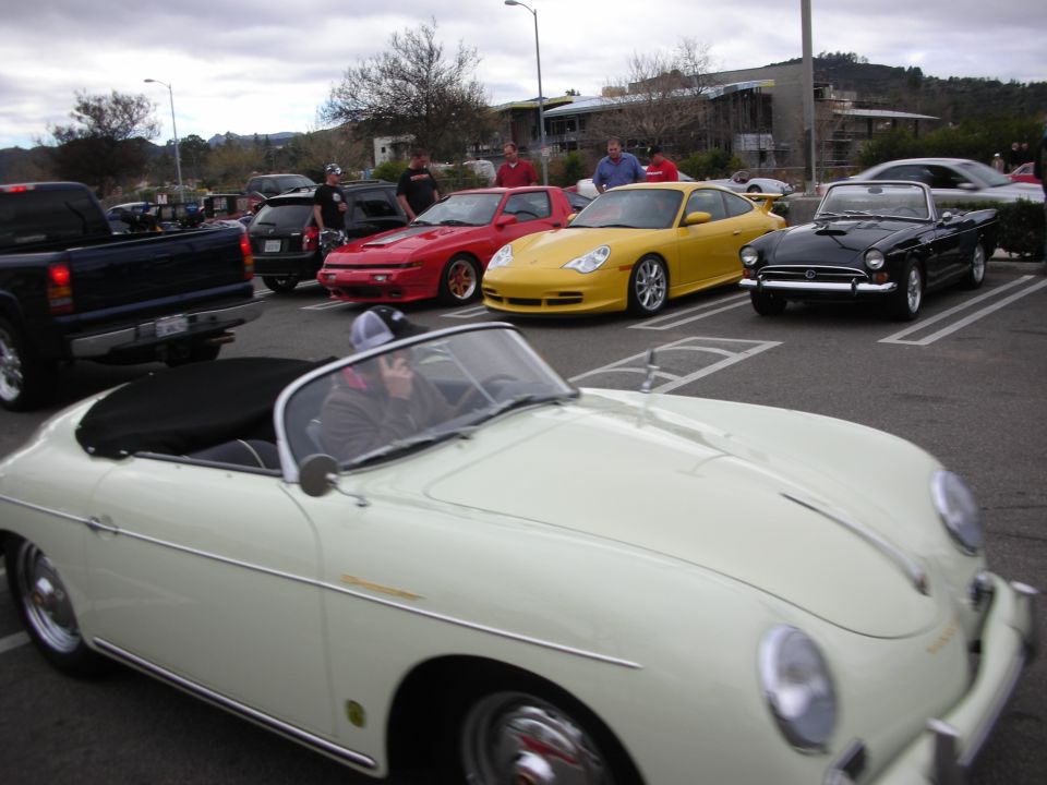 Cream Porsche 356 Speedster moving through a parking lot lined with sports cars