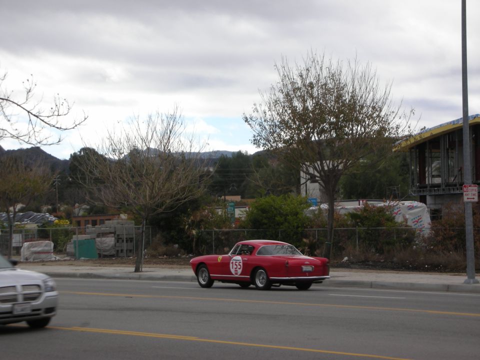 Red vintage Italian coupe with race number on a road by a chain-link fence