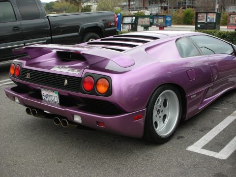 1998 Ford Crown Victoria - purple Lamborghini Diablo shows its rear wing, round taillights and twin exhausts while parked beside a pickup truck.