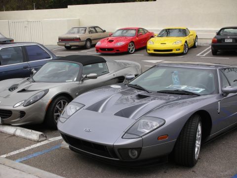 1998 Ford Crown Victoria - gray Ford GT with center stripes is parked beside a silver Lotus Elise, with a red Ferrari and yellow Corvette in the background.