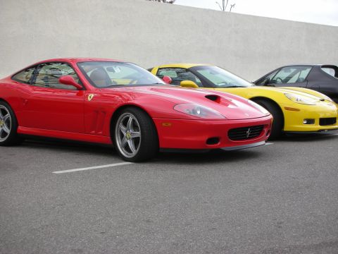 1998 Ford Crown Victoria - red Ferrari front-engine coupe with prancing-horse badge is parked beside a yellow Corvette against a plain wall.