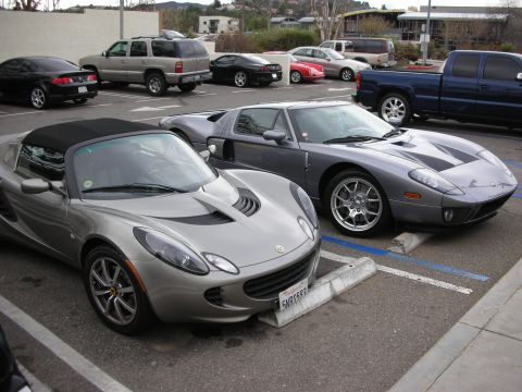 1998 Ford Crown Victoria - silver Lotus Elise convertible is parked beside a gray Ford GT, with SUVs and other sports cars filling the lot behind.