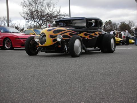 1998 Ford Crown Victoria - chopped black hot rod coupe painted with yellow and orange flames sits low on a parking lot, front suspension and wide rear tires exposed.