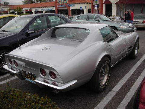 1998 Ford Crown Victoria - Rear three-quarter view of a silver Corvette C3 Stingray coupe with round taillights and rally wheels parked in a lot.