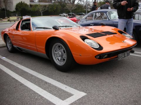 1998 Ford Crown Victoria - orange Lamborghini Miura with slatted rear deck and quad headlights sits low in a parking-lot show, wearing a European license plate.
