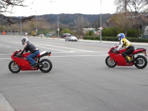 1998 Ford Crown Victoria - Two riders in helmets ride red sport motorcycles across a wide street with brown hills in the background.