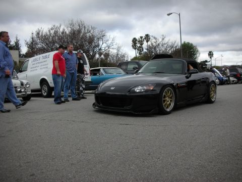 1998 Ford Crown Victoria - lowered black Honda S2000 roadster with gold wheels and a body kit sits at a parking-lot car meet as onlookers stand nearby.