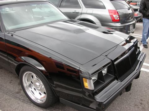 1998 Ford Crown Victoria - Front three-quarter view of a black Buick Grand National-style coupe with quad headlights and polished five-spoke wheels in a lot.
