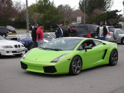 1998 Ford Crown Victoria - lime-green Lamborghini Gallardo with dark wheels drives on a street past a 40 mph sign and a crowd of onlookers.