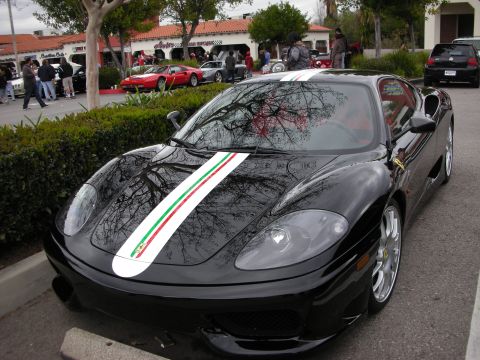 1998 Ford Crown Victoria - black Ferrari 360-style coupe with an Italian green-white-red center stripe parked by a hedge, with classic Ferraris in the background.
