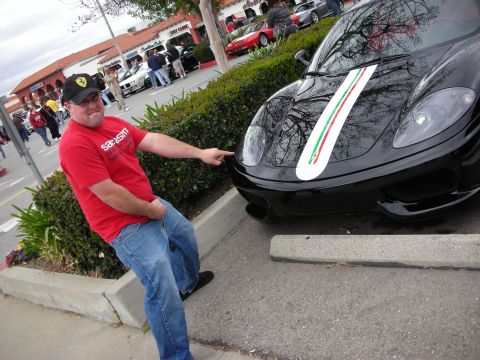 1998 Ford Crown Victoria - man in a red shirt and Ferrari cap points toward the nose of a black Ferrari coupe wearing an Italian tricolor stripe.