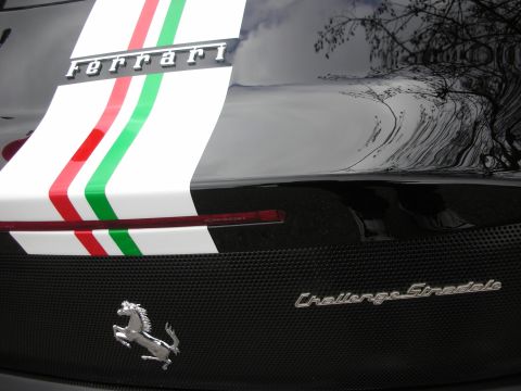 1998 Ford Crown Victoria - Close-up of a black Ferrari rear showing the prancing horse badge, carbon-fiber panel, 'ferrari' and 'Challenge Stradale' script, and a whi…