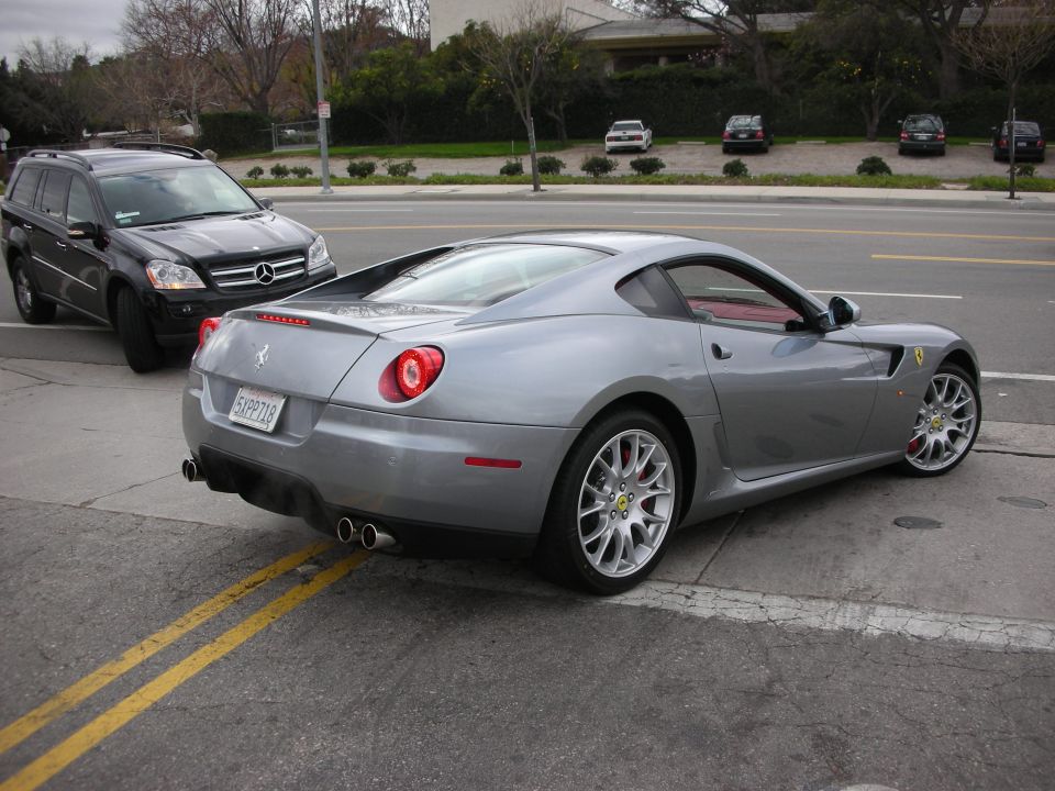 Rear three-quarter of silver Ferrari 599 coupe beside a black Mercedes SUV on a street