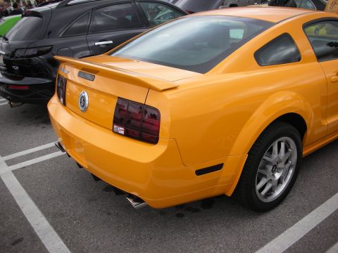 1998 Ford Crown Victoria - orange Ford Mustang coupe with a rear spoiler and five-spoke wheels parked in a striped lot beside darker cars.