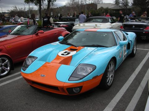 1998 Ford Crown Victoria - Ford GT in light blue and orange Gulf racing livery with a number 5 roundel sits among other cars at a packed car show.