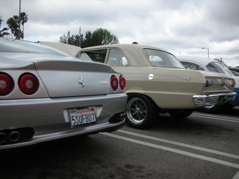 1998 Ford Crown Victoria - Rear view of a silver Ferrari with round taillights and prancing horse badge parked next to a tan vintage four-door at a car show.