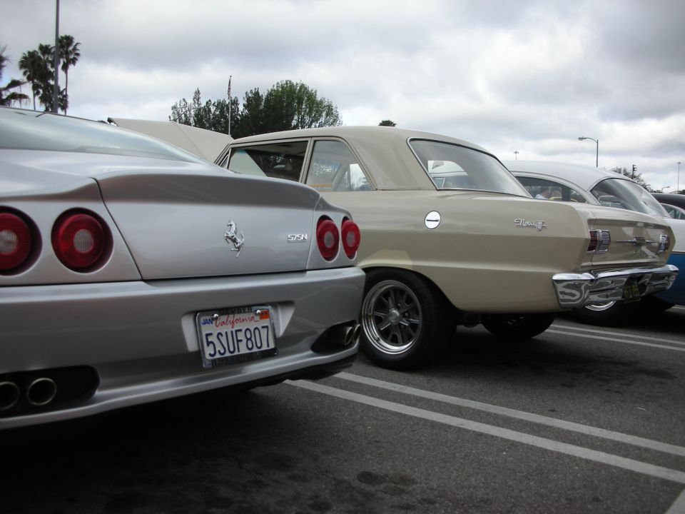 Rear of silver Ferrari 550/575 sedan beside a tan vintage sedan with California plate