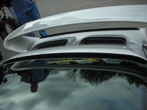 1998 Ford Crown Victoria - Detail shot of a silver sports car's rear wing and twin engine-cover vents, with a person and trees reflected in the bodywork.