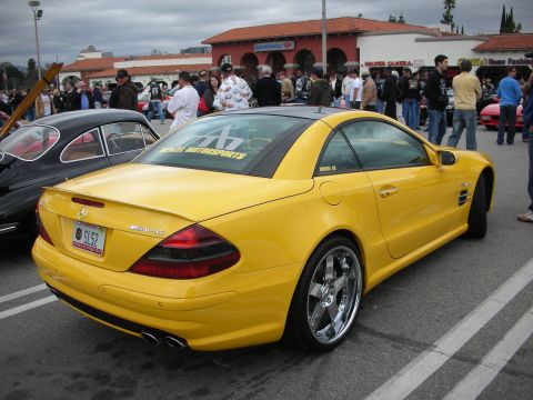 1998 Ford Crown Victoria - yellow Mercedes SL convertible with AMG badging and chrome wheels parked among spectators and cars at an outdoor show.