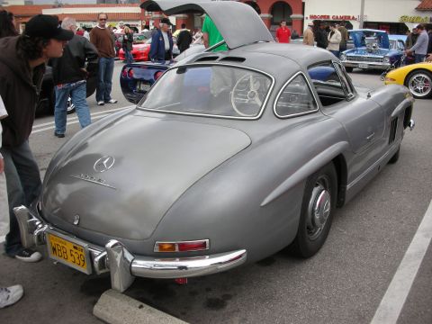 1998 Ford Crown Victoria - gray Mercedes 300SL Gullwing coupe with its door raised, parked among spectators and other cars at a show.