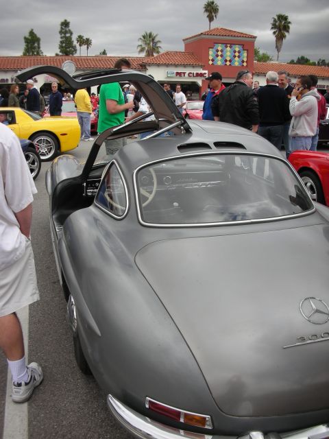 1998 Ford Crown Victoria - gray Mercedes 300SL Gullwing with its gull-wing door open, parked in a crowded lot in front of a pet clinic.