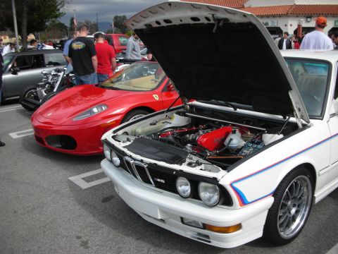 1998 Ford Crown Victoria - white BMW with M-stripes and its hood open showing the engine bay, parked next to a red Ferrari F430 at a show.
