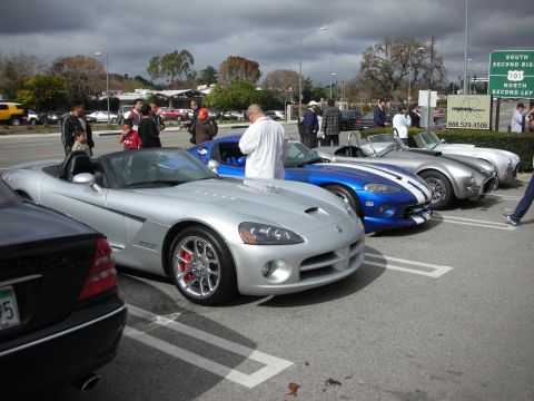 1998 Ford Crown Victoria - silver Dodge Viper convertible and a blue striped Viper sit in a row of sports cars under a cloudy sky at a car show.