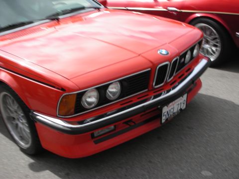 1998 Ford Crown Victoria - Close-up of the front end of a red BMW showing its quad round headlights, kidney grille, and chrome bumper.