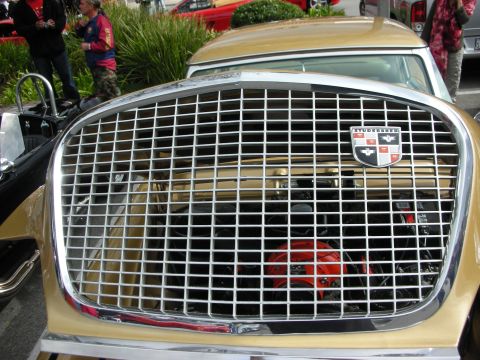 1998 Ford Crown Victoria - Detail of a gold classic Studebaker's chrome mesh grille bearing the Studebaker crest emblem at a car show.