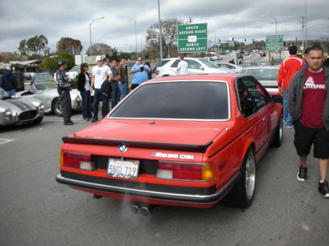 1998 Ford Crown Victoria - Rear three-quarter view of a red BMW M635CSi coupe with dual exhaust amid a crowd at a car meet.