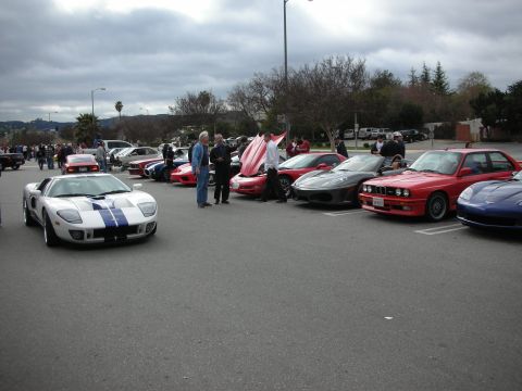 1998 Ford Crown Victoria - row of parked sports cars at an outdoor meet, led by a silver-and-blue Ford GT with a red BMW M3 down the line.
