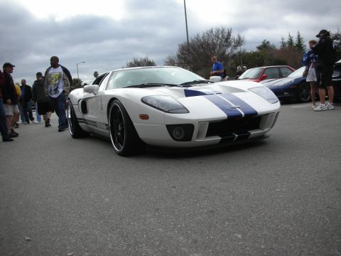 1998 Ford Crown Victoria - silver Ford GT with blue racing stripes and black wheels parked among spectators at a car gathering.