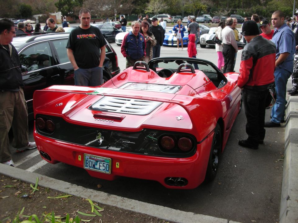 Rear of a red Ferrari F50 surrounded by spectators in a lot