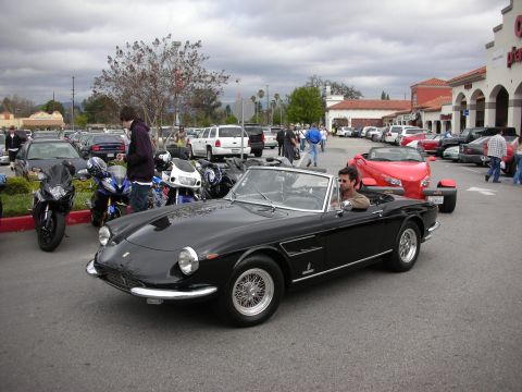 1998 Ford Crown Victoria - black vintage Ferrari convertible with chrome wire wheels driving through a parking lot at a car gathering.