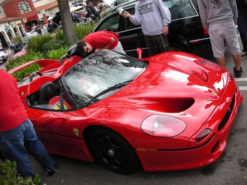 1998 Ford Crown Victoria - red Ferrari F50 with its roof panel removed while a man leans over the cockpit in a shopping-center lot.