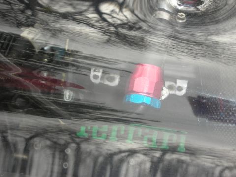 1998 Ford Crown Victoria - glossy reflective surface showing green Ferrari script lettering and a red-and-blue threaded hose fitting.
