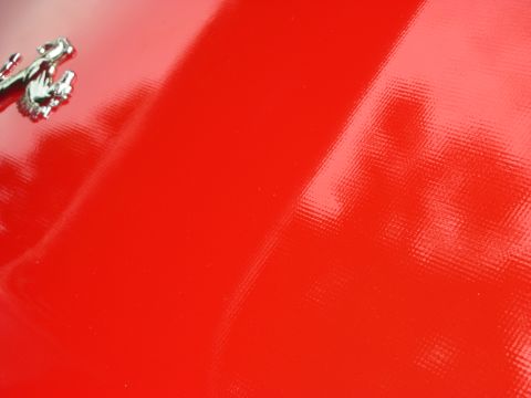 1998 Ford Crown Victoria - Extreme close-up of glossy red Ferrari bodywork with the chrome prancing-horse emblem in the corner.