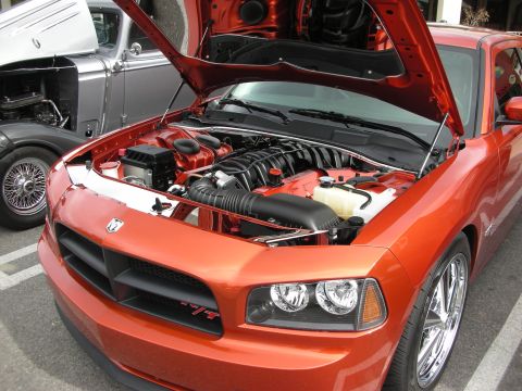 1998 Ford Crown Victoria - Open hood reveals the engine bay of an orange Dodge Charger R/T with chrome wheels at an outdoor car show.