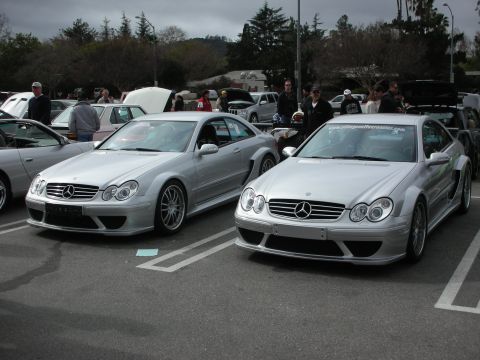 1998 Ford Crown Victoria - pair of silver Mercedes-Benz CLK AMG coupes parked side by side in a lot crowded with spectators at a car show.
