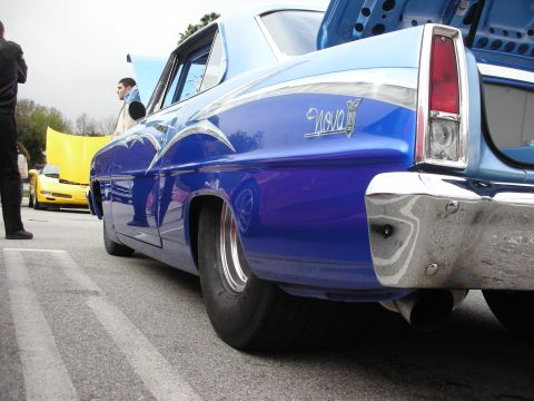 1998 Ford Crown Victoria - Low-angle rear-quarter shot of a blue Chevrolet Nova with Nova script and a wide rear tire at a car show.