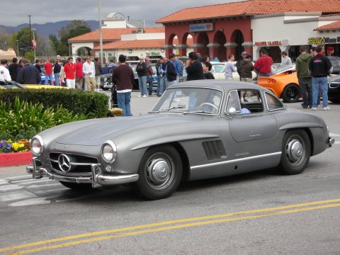 1998 Ford Crown Victoria - silver Mercedes-Benz 300SL Gullwing coupe sits on a street lined with spectators at an outdoor car gathering.