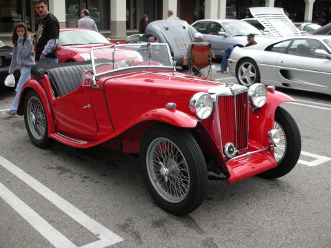 1998 Ford Crown Victoria - red vintage MG TC roadster with chrome wire wheels and upright grille parked among cars at a show.
