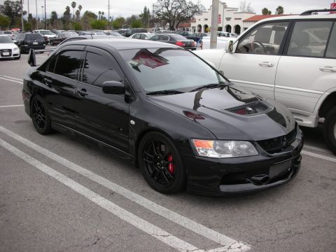 1998 Ford Crown Victoria - black Mitsubishi Lancer Evolution sedan with a vented hood, black wheels and red brake calipers parked in a lot beside other cars.