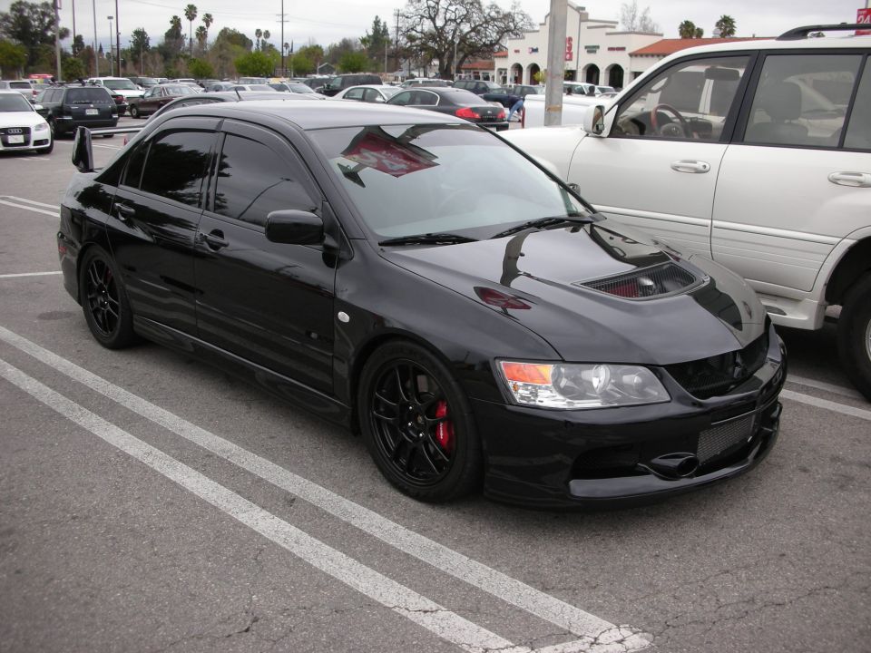 Black Mitsubishi Lancer Evolution sedan with black wheels and red brake calipers in a parking lot