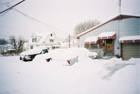 1989 Ford LTD Crown Victoria - Snapshot of a residential driveway after a heavy snowstorm, with a dark sedan buried to its beltline in snow beside a second vehicle covere…