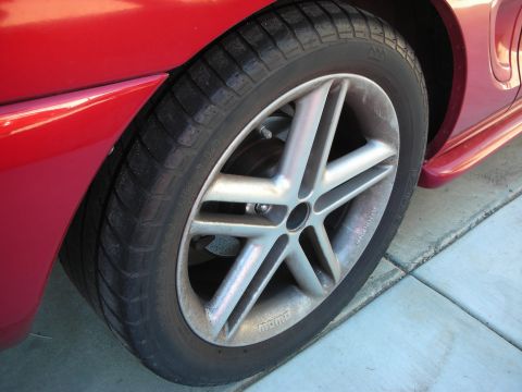 1998 Ford Crown Victoria - Close-up of a red car's silver five-spoke alloy wheel and low-profile tire on a concrete driveway.