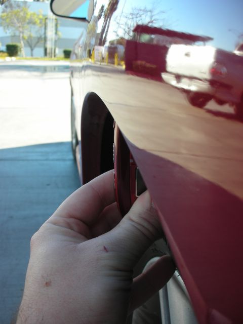 1998 Ford Crown Victoria - hand holds a phone alongside the lowered side body and wheel well of a red car in a sunny parking lot.